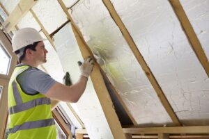 Construction worker in a high-visibility vest installing reflective insulation boards in a loft or roof space