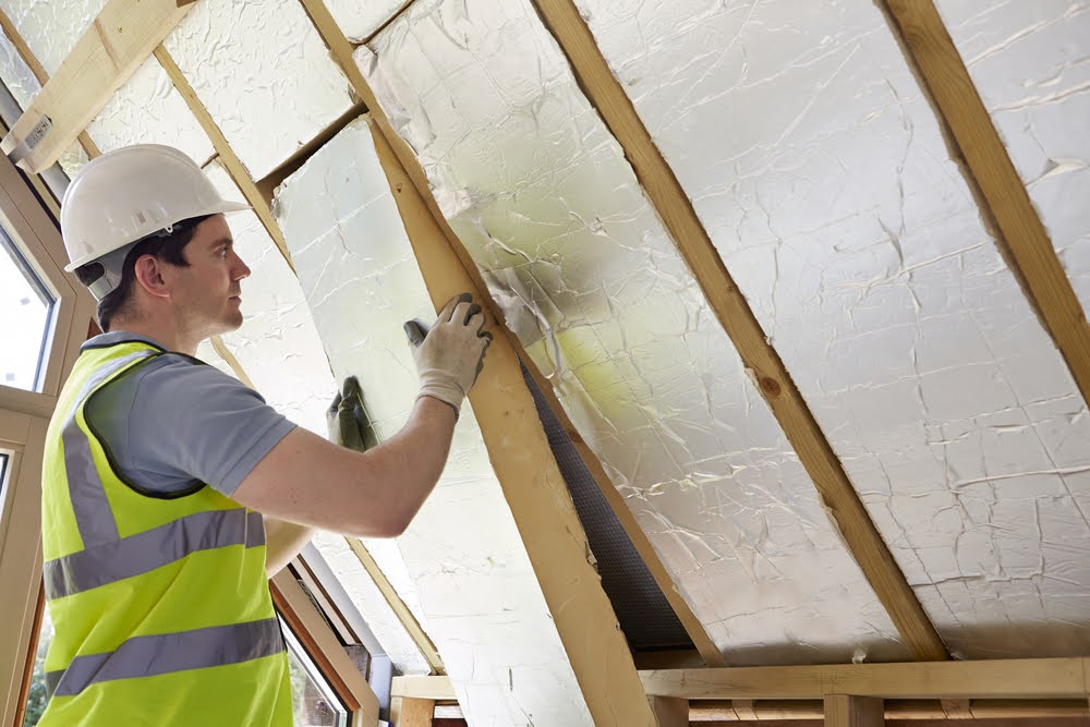 Construction worker fitting reflective insulation panels between roof rafters in a loft conversion project