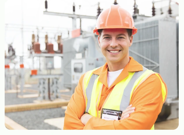Engineer wearing an orange hard hat and high-visibility vest smiling at an electrical substation site