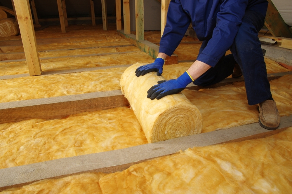 Man installing thermal insulation layer under the roof, using mineral glass wool