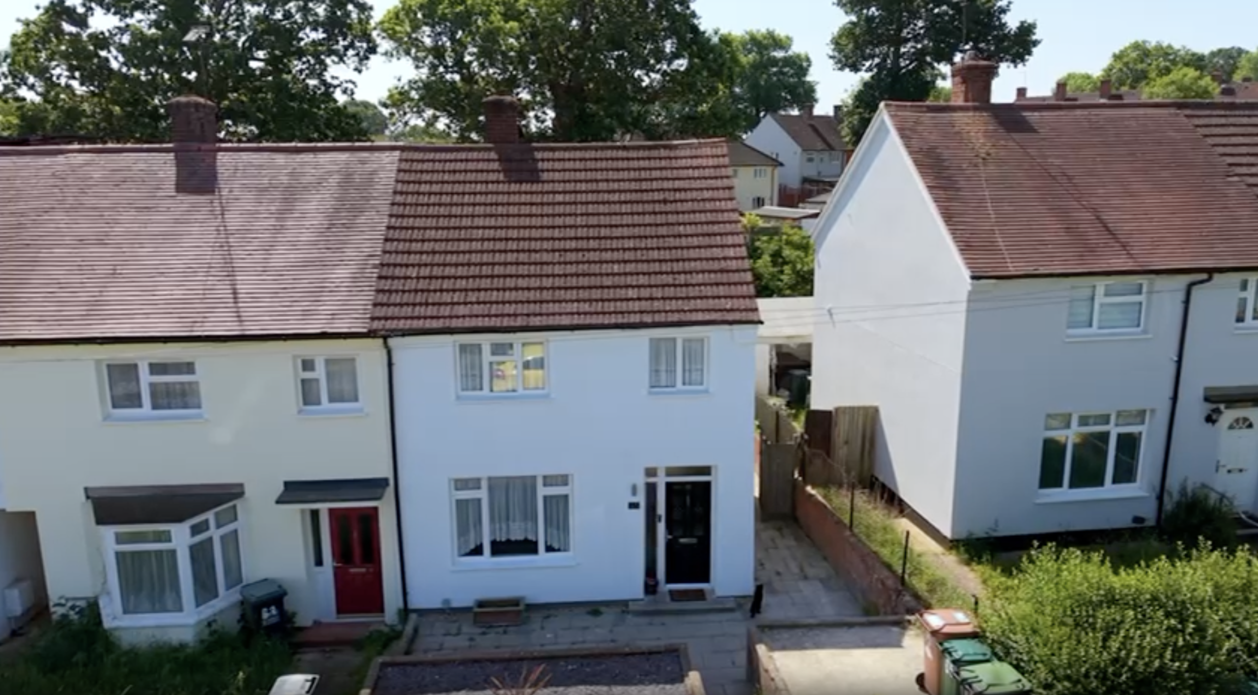 A two-story semi-detached white house with a brown tiled roof and a black front door next to a narrow side path.