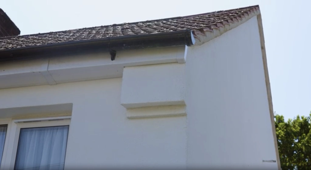 Close-up view of a freshly rendered white external wall insulation system installed on a house in South Oxhey, showcasing the clean finish around the roofline, guttering, and window frame.