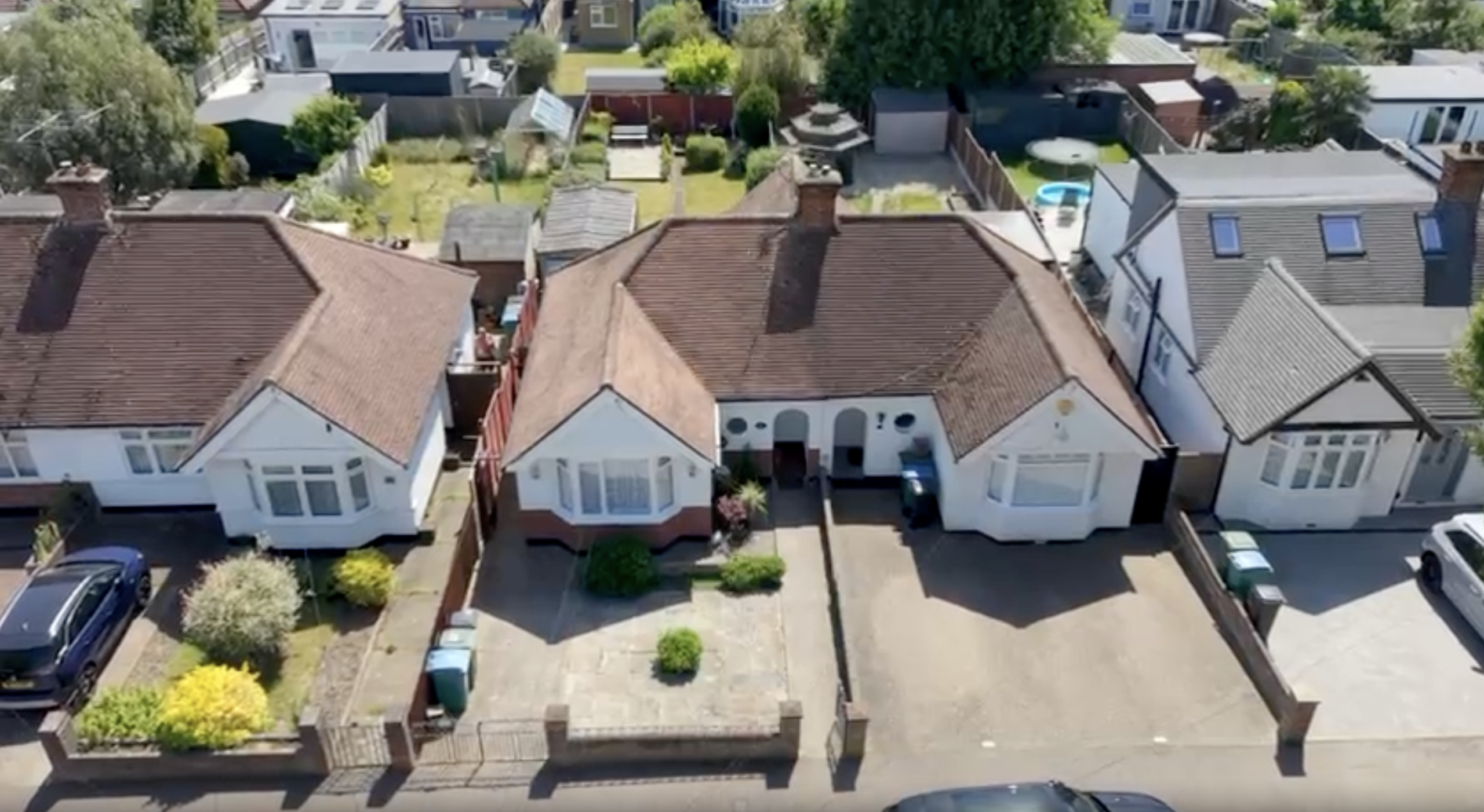 An aerial view of suburban semi-detached bungalows with brown tiled roofs, brick driveways, and front gardens.