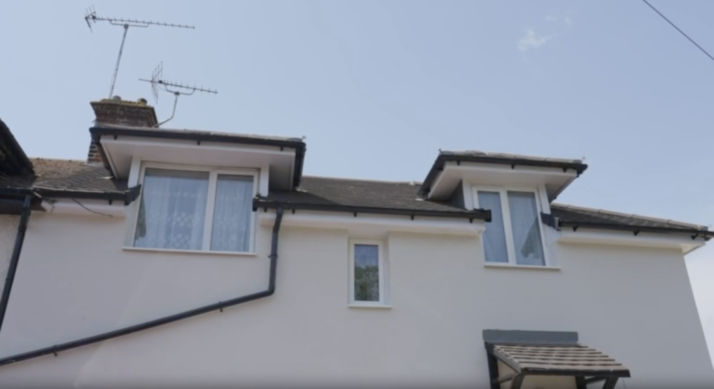 An external view of the upper story of a house with freshly rendered, off-white external wall insulation.